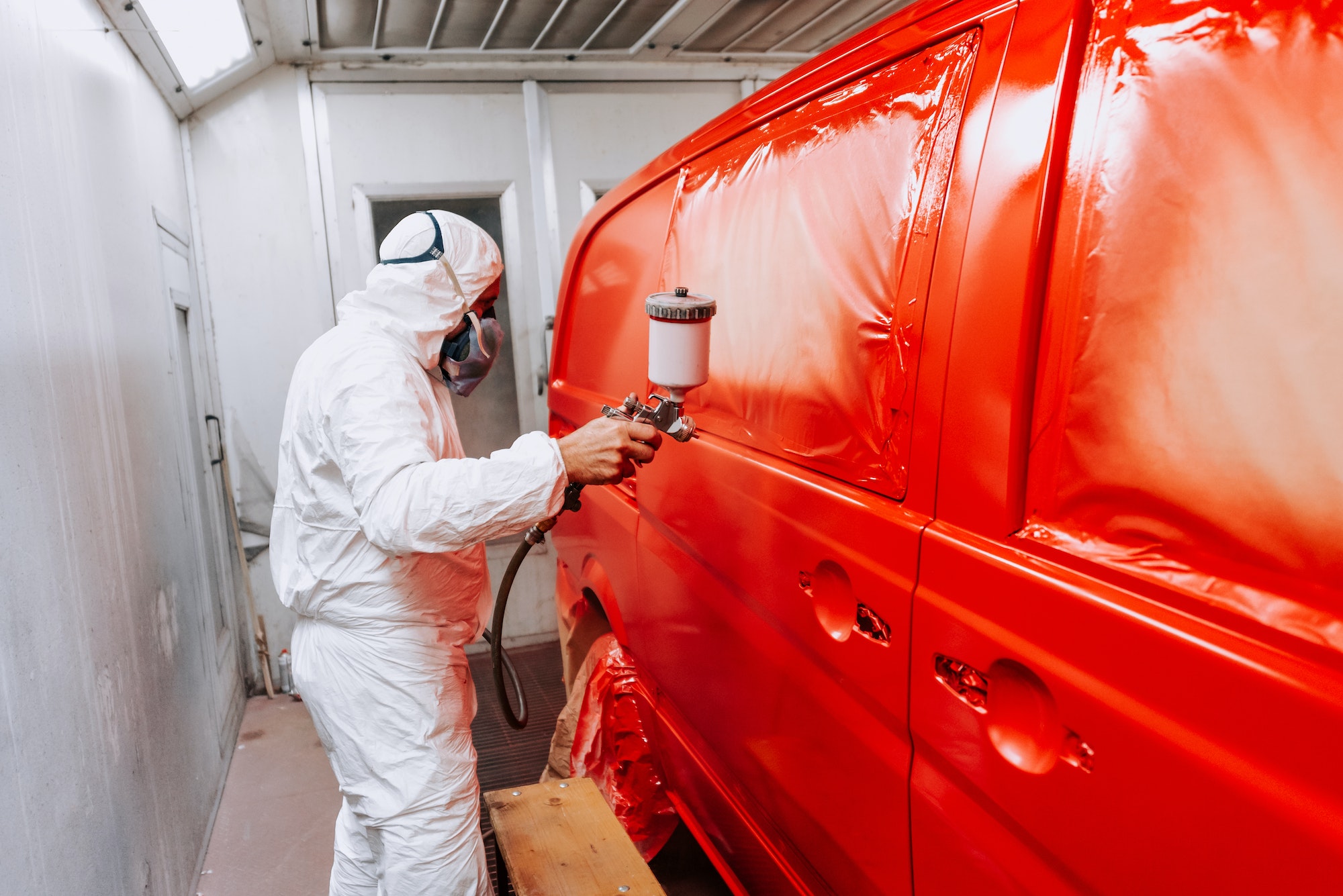 Auto mechanic working and painting a red van in a special booth