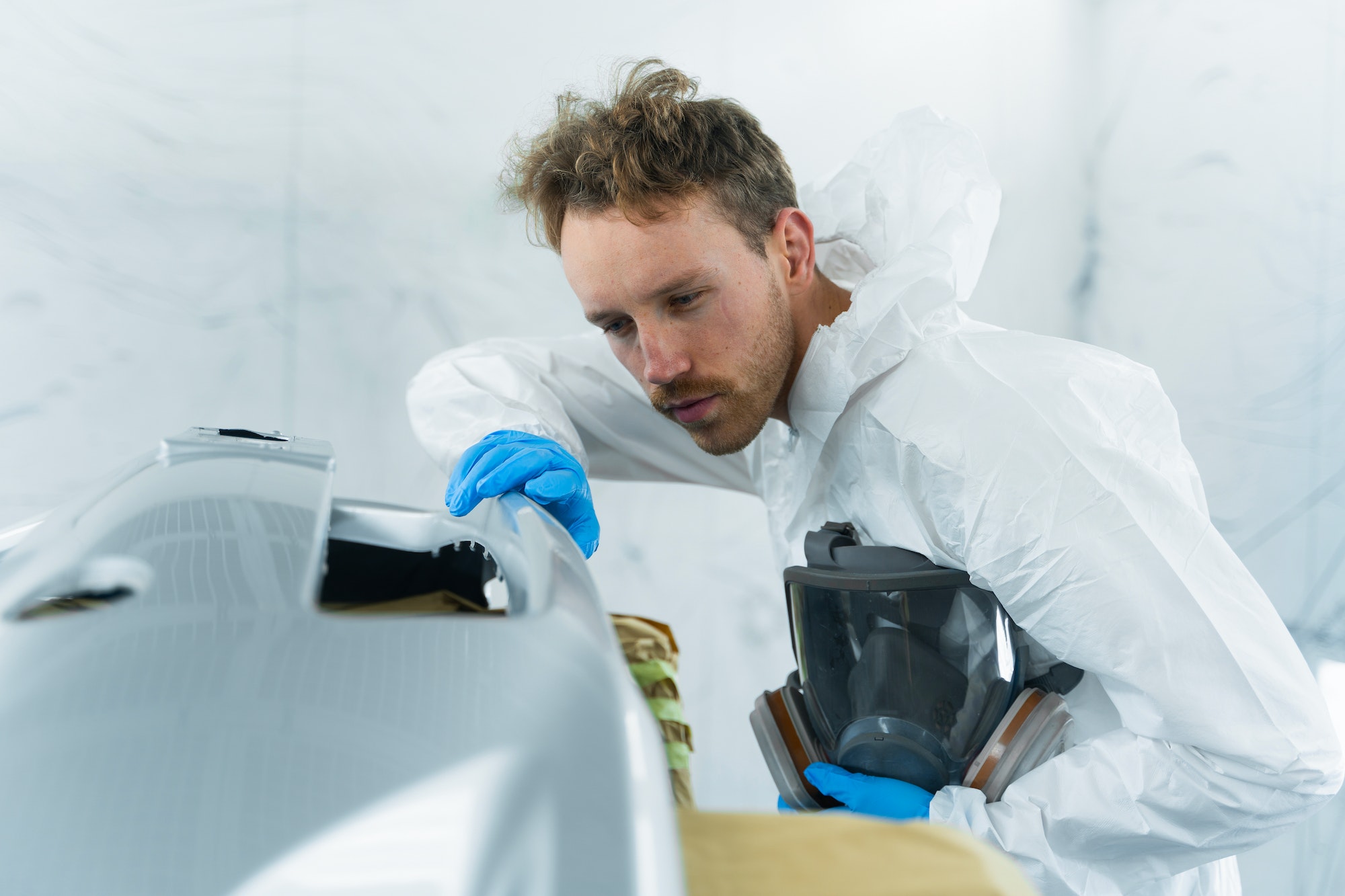 Young car painter examines the surface of the car bumper in detail for the quality of the paintwork